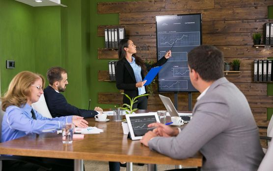 Business woman in a conference room holding a presentation with charts on tv screen
