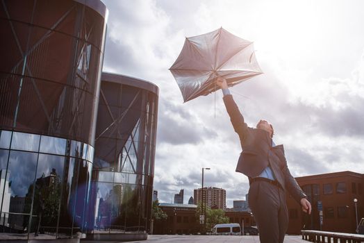 Life hasnt been kind lately. Shot of a businessman holding an umbrella being broken by the wind.
