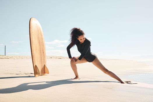 Surfing is attitude dancing. Shot of a young woman stretching on the beach.