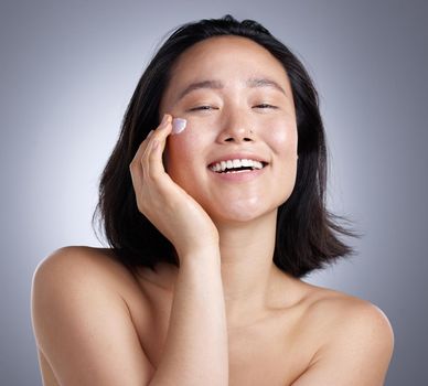 Keep your skin happy. Shot of a young woman applying lotion against a grey background.