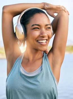 One active latina woman stretching arms and triceps by pulling elbow towards spine while exercising outdoors. Female athlete doing warm up to prepare body and muscles for training workout or run while listening to music on wireless headphones