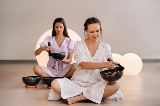 Two female yoga teachers playing a Tibetan bowl in the gym during a yoga retreat