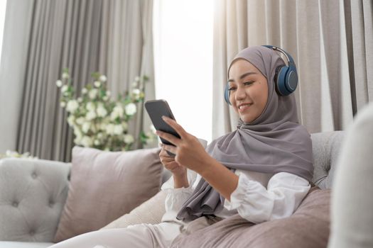 Portrait of beautiful asian muslim female in sleepwear watching online story on mobile phone, lites on bed and connected with wireless internet. Young cute girl with hijab listen music from smartphone