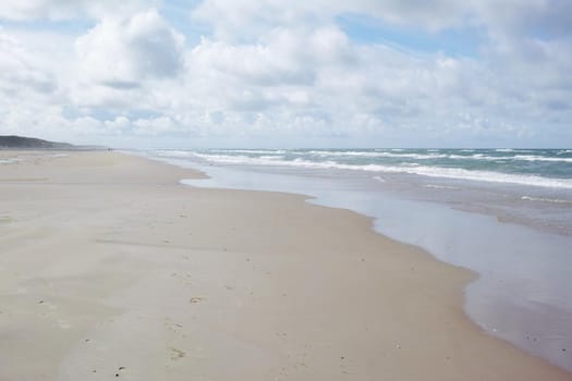 An empty beach on a cloudy morning with copyspace. Ocean waves washing onto a sandy shore, calm, peaceful day in relaxing zen environment. Copy space at sea with clouds in the sky in the background