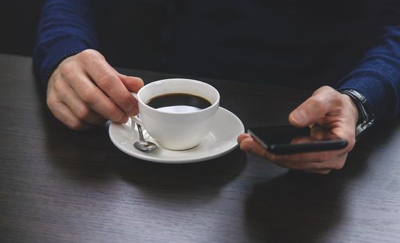 A man at a table with a phone and a cup of coffee. Selective focus. People.