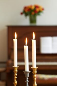 Burning candles in a cosy room against a blurry background. Lighting a candle symbolizes hope and faith in religion. Candle lights in gold and silver holders, for a wedding, funeral home, or church