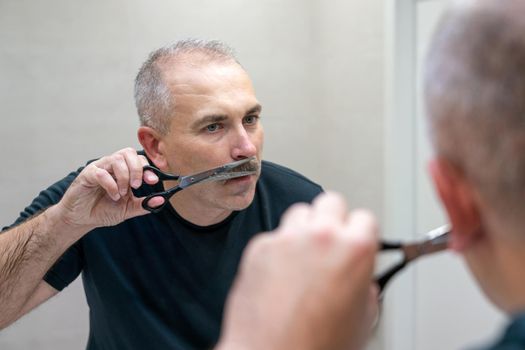 Middle-aged handsome man using scissors to cut his mustache