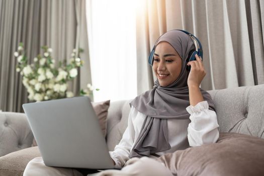 Asian muslim woman having video teleconference on her laptop at home, online learning or working from home concept
