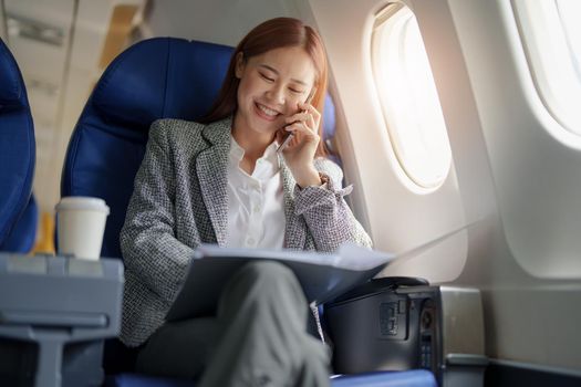 portrait of A successful asian business woman or female entrepreneur in formal suit in a plane sits in a business class seat and uses smartphone with documents for work during flight
