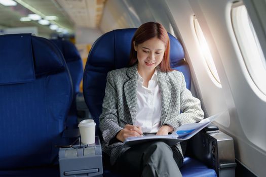 portrait of A successful asian business woman or female entrepreneur in formal suit in a plane sits in a business class seat and uses a pen with documents for work during flight