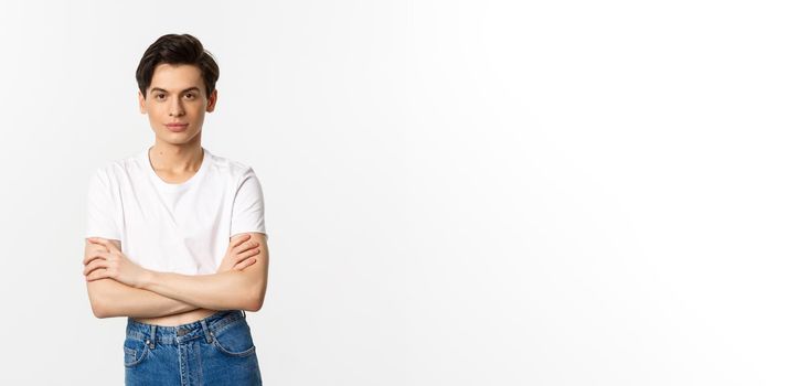 Image of sassy gay man in crop top smiling, looking confident, cross arms on chest and standing over white background