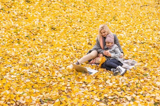 beautiful mother and kid girl playing at laptop outdoors in fall