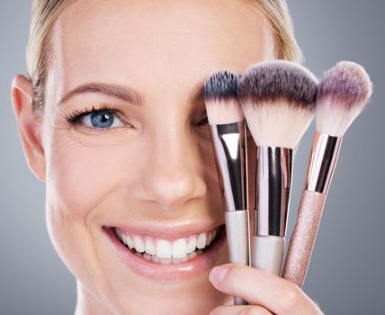 Theres nothing wrong with a little appearance enhancement. Studio portrait of an attractive mature woman holding a collection of makeup brushes against a grey background.