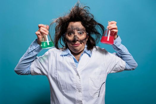 Goofy looking wacky scientist with messy hairstyle and dirty face holding professional Erlenmeyer glass jars