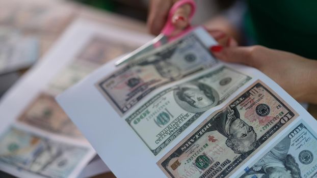 Female hands cutting out dollar bills printed on printer with scissors closeup