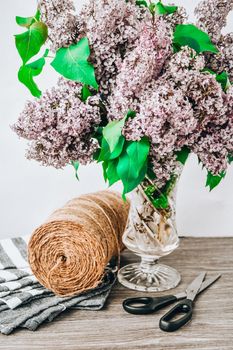 Lilac spring bouquet in glass vase on table with scissors and rope