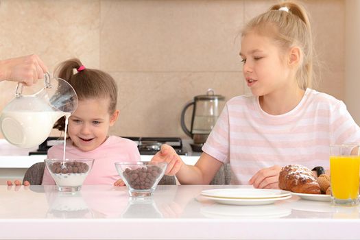 Mother serving breakfast to her two daughters at a table in kitchen, happy single mother concept