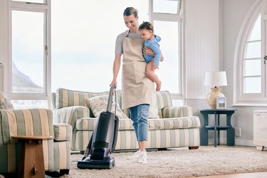 Only moms know how to juggle everything with one hand. Shot of a mom vacuuming the living room with her baby on her arm.