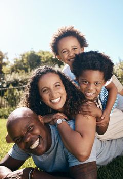 Happy african american family of four lying stacked on top of each other while having fun and playing together in the sun. Carefree mother and two kids piled on top of father while bonding at the park
