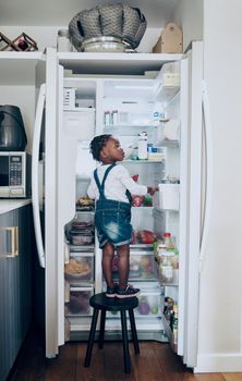 Snack time. Shot of a toddler taking food from the fridge at home.