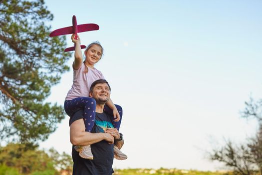 Cute girl riding on father's shoulder playing with toy airplane