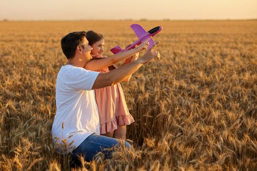 Cute girl playing with toy airplane against sky in wheat field