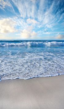 Sandy beach, sea, blue sky with clouds and copy space. Scenic seascape view of ocean waves washing on shore sand in a tropical resort with copyspace. Travel overseas, tourism abroad on summer holiday