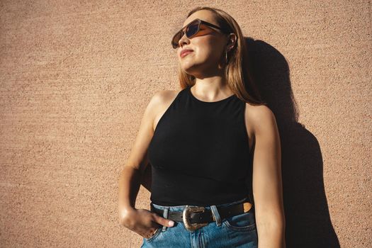 The blonde model wearing sunglasses stands against the beige wall