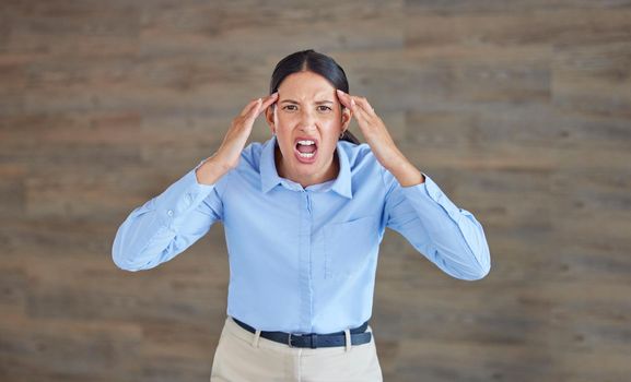 Young mixed race woman looking angry and annoyed while screaming and expressing rage at work. Hispanic female having a mental breakdown while standing in an office against a copyspace wall