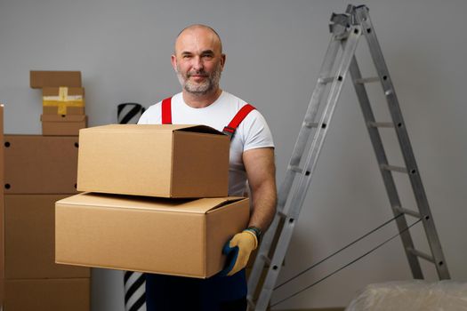 Middle-aged man mover in uniform holding cardboard box, portrait