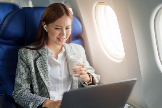 portrait of A successful asian businesswoman or female entrepreneur in formal suit in a plane sits in a business class seat and uses a computer laptop during flight