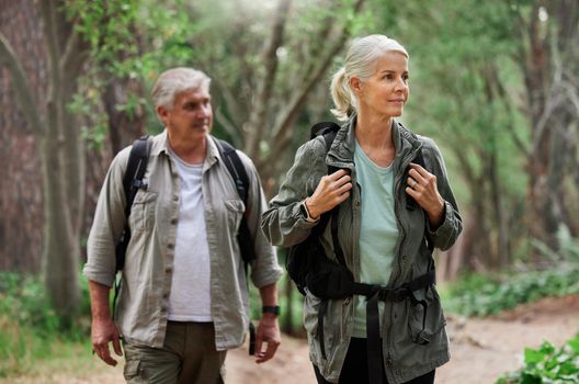 A mature caucasian couple out for a hike together. Senior man and woman smiling and walking in a forest in nature