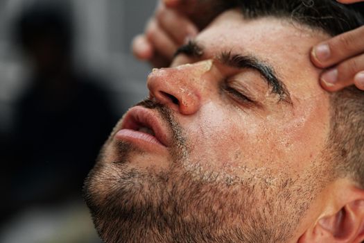 Relaxed man having purifying mask on face in a barbershop