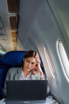 portrait of A successful asian businesswoman or female entrepreneur in formal suit in a plane sits in a business class seat and uses a computer laptop during flight
