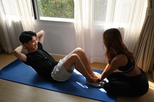Healthy young Asian couple exercising on fitness mat in living room.