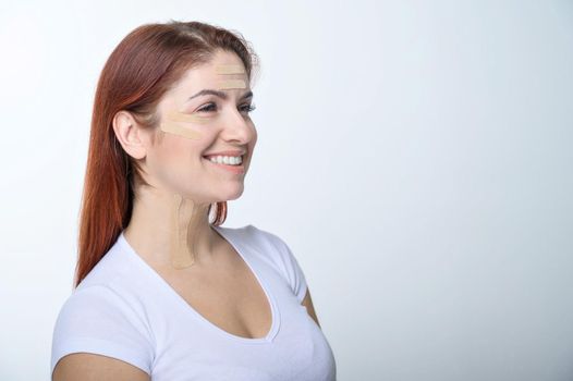 Portrait of a redhead woman with tapes on skin color face for rejuvenation. An alternative way to fight wrinkles.
