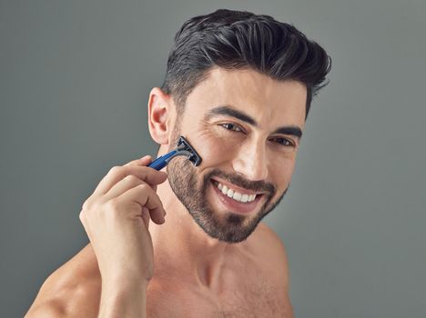 What do you have in your beard grooming kit. Shot of a handsome young man shaving his beard while standing against a grey background.