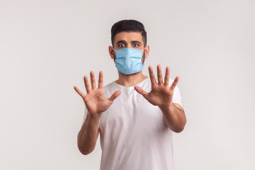 Alarming scared panicking man in hygienic mask gesturing stop, afraid of coronavirus infection