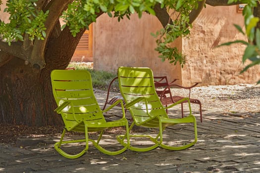 Two green vintage courtyard rocking chairs under a shady tree in a secluded and private garden at home. Patio furniture and seating set to enjoy and relax in summer. Lounging and feeling cosy outside