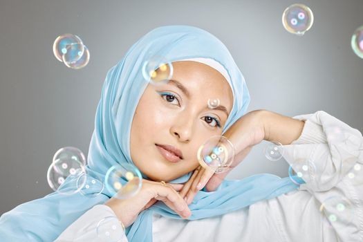 Portrait of a beautiful muslim woman wearing blue hijab headscarf against grey background. Arab female in a happy daydream and fantasy surrounded by the pure delight and innocence of playful bubbles