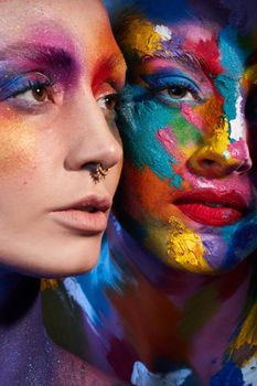 Life isnt all black and white. Studio shot of two young women posing with multi-coloured paint on her face.