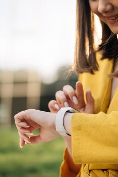 Appealing young elegant woman touching a smartwatch. Caucasian woman use her wearable smart watch and smiling. Smart watch. Smart watch on a woman's hand outdoor
