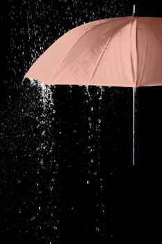 Pink umbrella under raindrops with black background