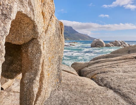 A rocky shore and a seascape view of the ocean with blue sky copy space and a mountain in the background in Camps Bay, Cape Town, South Africa. Calm, serene, tranquil beach and nature scenery