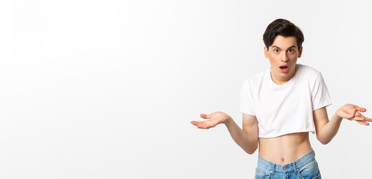 Lgbtq community. Confused gay man in crop top shrugging and staring at camera, cant understand, standing over white background