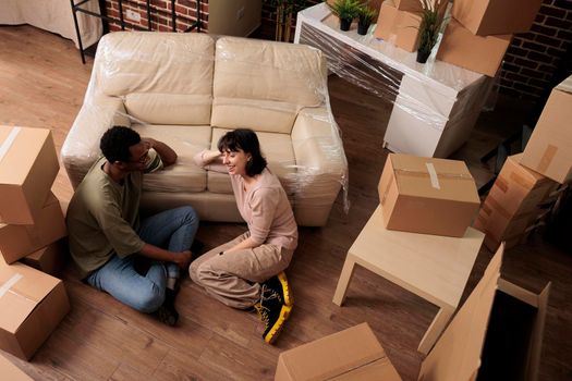 Diverse married couple sitting on apartment floor and enjoying relocation