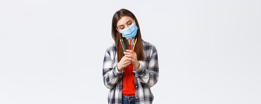Social distancing, leisure and hobbies on covid-19 outbreak, coronavirus concept. Thoughtful cute, dreamy woman in medical mask decide which colored pencil choose, pondering what draw