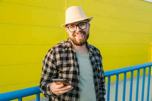Bearded hipster guy in glasses using smartphone technology for making online booking and banking during travel vacations - millennial blogger with beard messaging in social networks in street