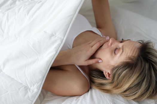 Woman looks in shock under covers in bed