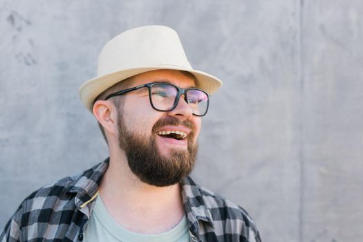 Portrait of positive young hipster man smiling over yellow wall store outdoor background - Handsome trendy bearded guy with hat and glasses standing outdoors - Fashion and trendy youth people concept